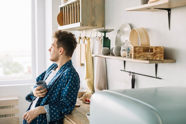 Hombre apoyado en el mostrador de la cocina con taza de café