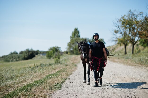 Hombre árabe de barba alta con casco negro con caballo árabe