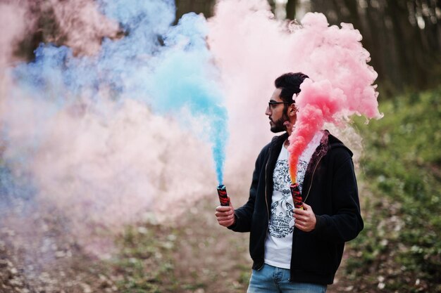 Hombre árabe de estilo callejero con anteojos sostiene una bengala con una bomba de granada de humo roja y azul