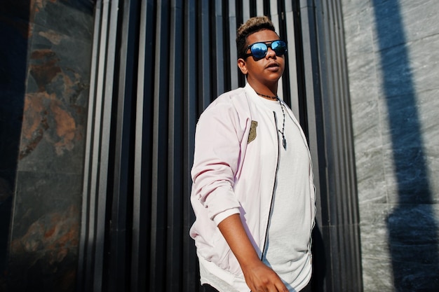 Hombre árabe con estilo hipster en gafas de sol posó al aire libre en la calle al atardecer contra la pared gris