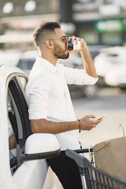 El hombre árabe usa un teléfono inteligente mientras espera cargar la batería en el automóvil.