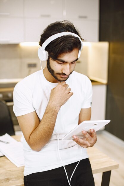 Hombre árabe viendo seminarios web en línea, sentado en una cocina con una tableta disfrutando de la educación a distancia
