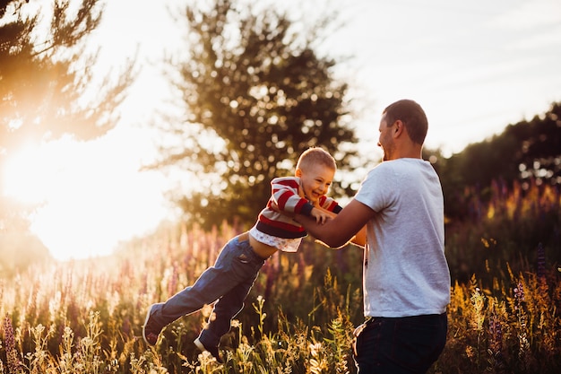 El hombre arroja a su hijo posando en el campo en las luces del sol de la tarde