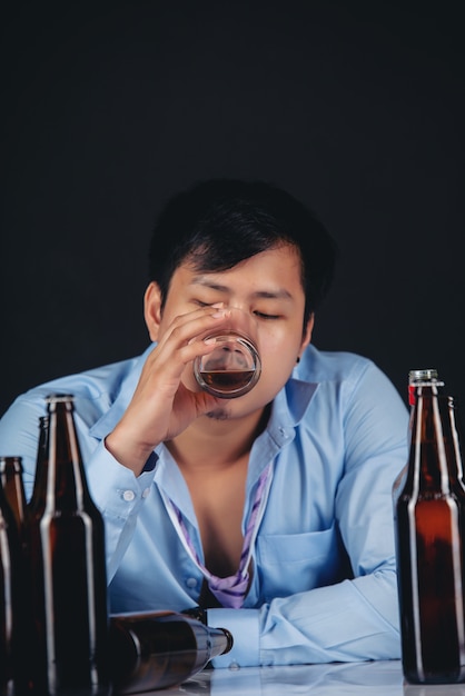 Hombre asiático alcohólico bebiendo whisky con muchas botellas