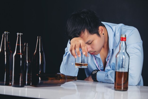 Hombre asiático alcohólico bebiendo whisky con muchas botellas