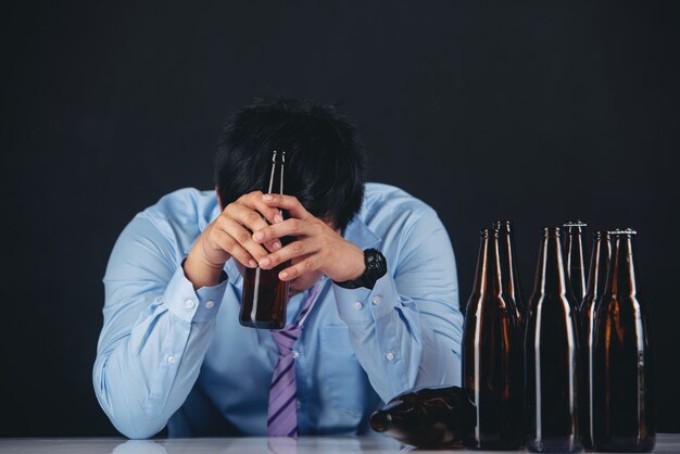 hombre asiático alcohólico con muchas botellas de cerveza