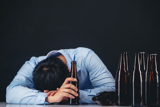 hombre asiático alcohólico con muchas botellas de cerveza