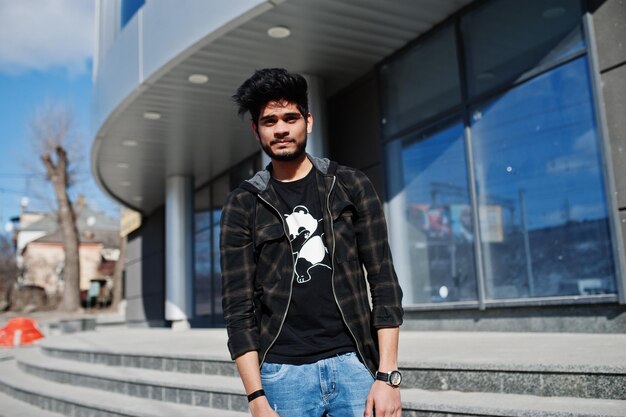 Hombre asiático con barba en ropa informal posando contra un nuevo edificio moderno