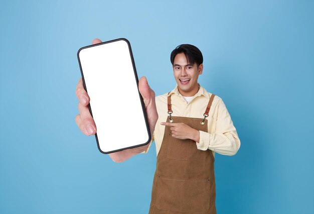 Hombre asiático barista feliz mostrando una maqueta de teléfono inteligente apuntando con el dedo a una pantalla en blanco en una cafetería