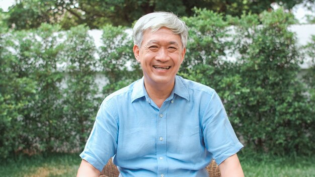 Hombre asiático chino del retrato que siente feliz sonriendo en casa. Un varón más viejo relaja la sonrisa dentuda que mira mientras que miente en el jardín en casa en el concepto de la mañana.