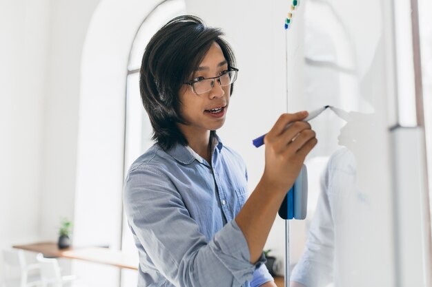 Hombre asiático concentrado en camisa azul con rotafolio y marcador para el trabajo
