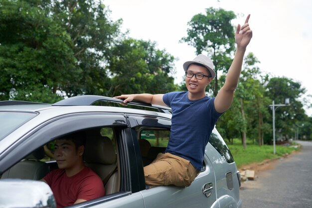 Hombre asiático conduciendo coche y alegre amigo sentado en la ventana de la puerta trasera