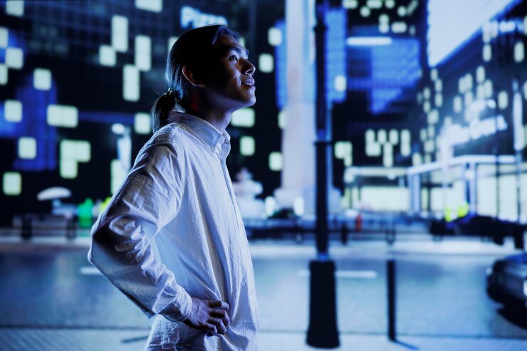 Foto gratuito hombre asiático deambulando por los bulevares de la ciudad durante la noche, sorprendido por los edificios del paisaje urbano. ciudadano paseando por avenidas vacías por la noche, disfrutando de los alrededores iluminados por las farolas