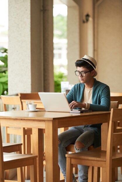 Hombre asiático elegante joven sentado en la mesa de café y trabajando en la computadora portátil