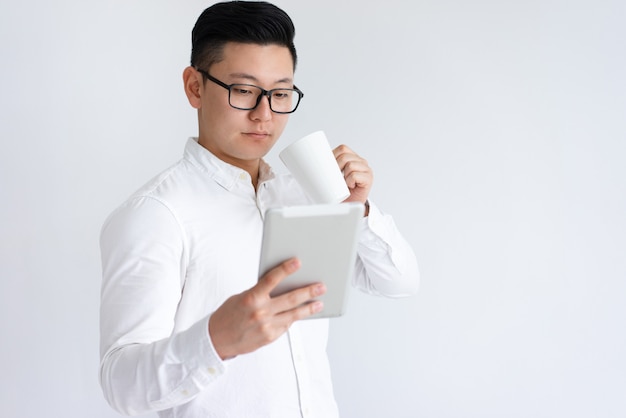 Hombre asiático enfocado que usa la tableta y tomando café