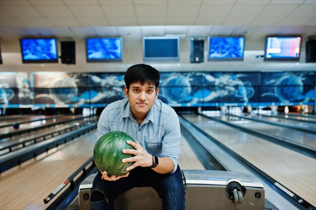 Hombre asiático con estilo en camisa de jeans de pie en la bolera con la pelota en la mano