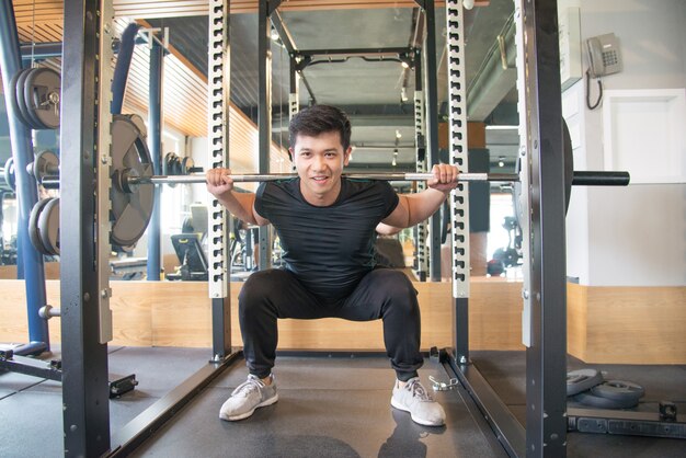 Hombre asiático fuerte que coloca y que levanta la barra en gimnasio