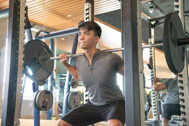 Hombre asiático fuerte serio que coloca y que levanta la barra en gimnasio