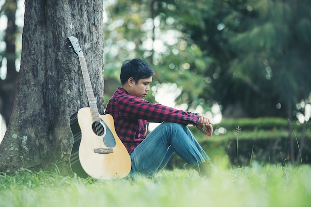 Hombre asiático con guitarra acústica en un parque