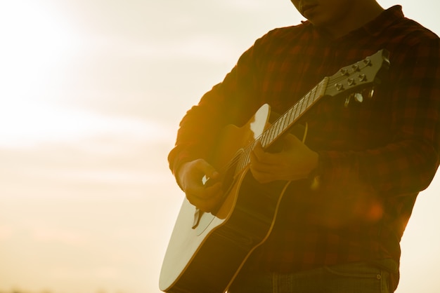 Hombre asiático con guitarra acústica durante una puesta de sol