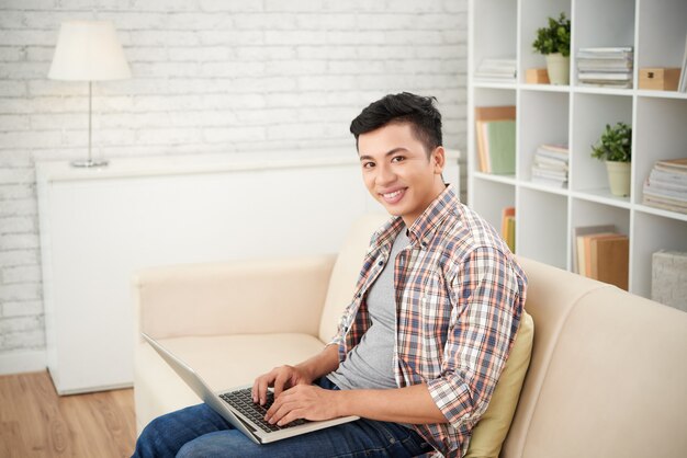 Hombre asiático haciendo trabajo independiente en la computadora portátil Siiting en el sofá en casa