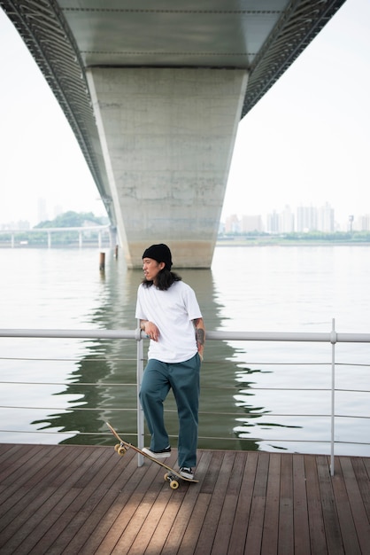 Hombre asiático joven andar en monopatín en la ciudad al aire libre