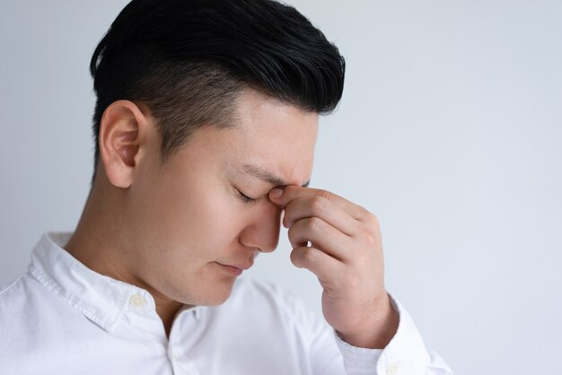 Hombre asiático joven cansado que toca su puente de la nariz