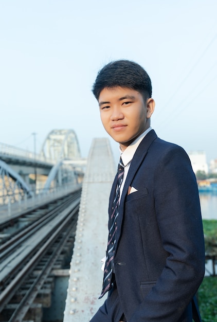 Hombre asiático joven confidente en un traje apoyado en un puente