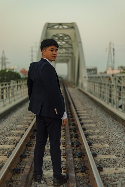 Hombre asiático joven confidente en un traje de pie en medio de un ferrocarril mirando hacia atrás