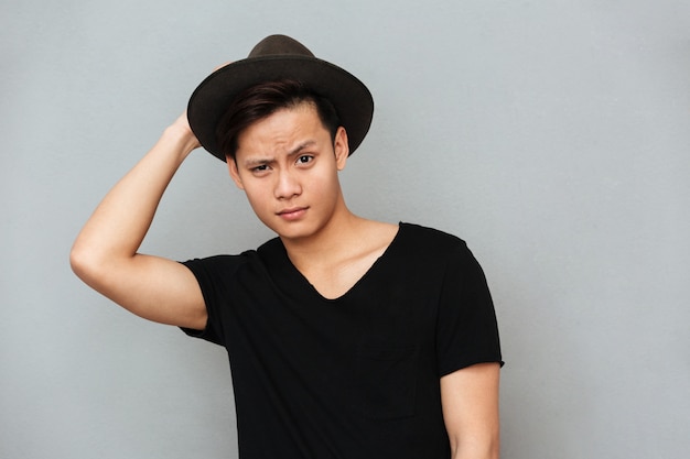 Hombre asiático joven hermoso que se coloca aislado sobre la pared gris