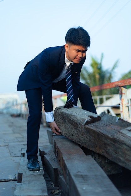 Hombre asiático joven en un traje que hace esfuerzo mientras levanta un tronco