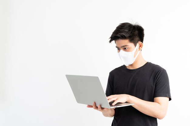 Hombre asiático con mascarilla para proteger el coronavirus covid-19 usando una computadora portátil en la sala de cuarentena, póngase en cuarentena para proteger la propagación del coronavirus Covid-19