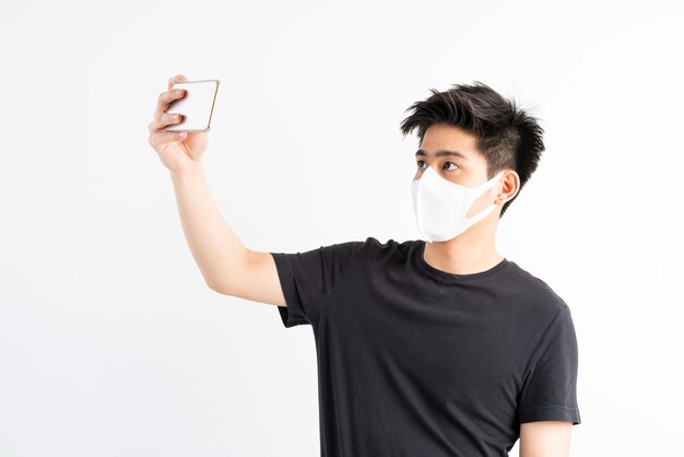 Hombre asiático con mascarilla para proteger el coronavirus covid-19 usando un teléfono inteligente en la sala de cuarentena