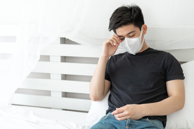 Hombre asiático con mascarilla para protegerse la sensación de dolor de cabeza y tos debido al coronavirus covid-19 en la sala de cuarentena
