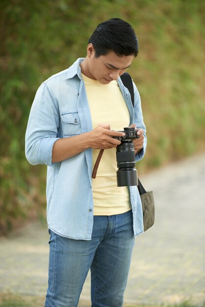 Hombre asiático de pie en el parque y revisando fotos en la cámara