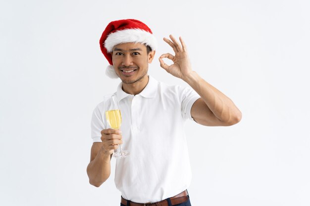Hombre asiático que muestra la muestra ACEPTABLE y que sostiene el cubilete con champán