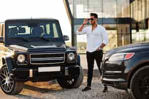 Foto gratuita un hombre asiático sólido con camisa blanca y gafas de sol posó cerca de autos todoterreno de la mafia negra