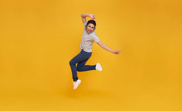Hombre asiático sonriendo y saltando con auriculares inalámbricos escuchando música