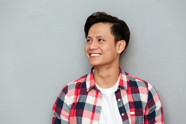 Hombre asiático sonriente de los jóvenes que se coloca sobre la pared gris.