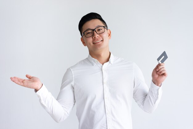 Hombre asiático sonriente que sostiene la tarjeta de crédito y que levanta la mano