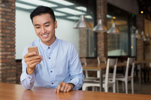 Hombre asiático sonriente que usa smartphone en el vector del café