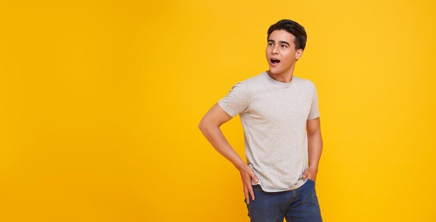 Hombre asiático sorprendido y conmocionado que cubre la boca aislado en el espacio de copia de fondo de estudio amarillo