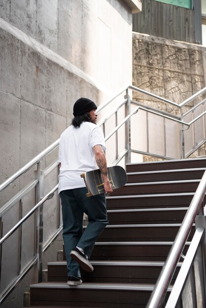 Hombre asiático sosteniendo su patineta mientras camina por las escaleras