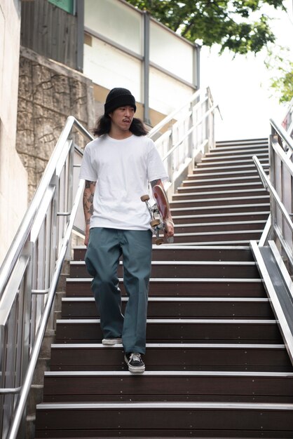 Hombre asiático sosteniendo su patineta mientras camina por las escaleras