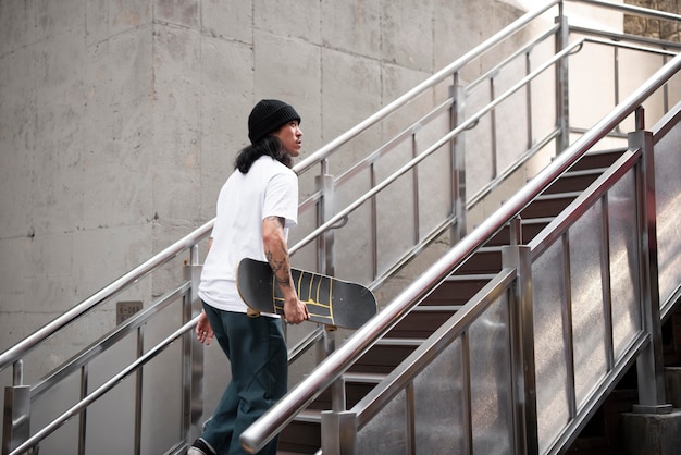 Hombre asiático sosteniendo su patineta mientras camina por las escaleras