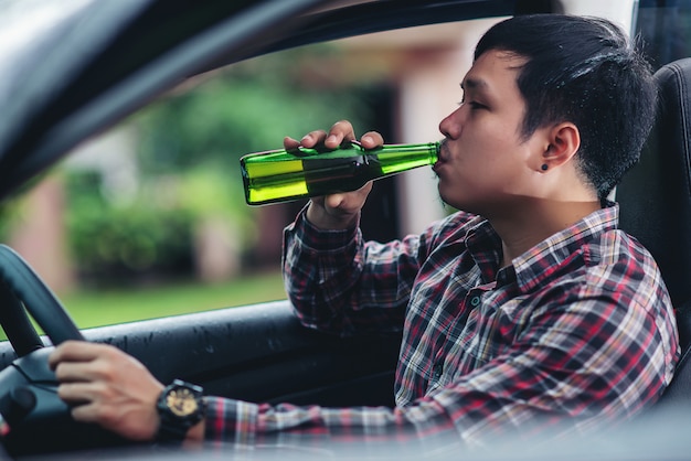 Hombre asiático sostiene una botella de cerveza mientras conduce un automóvil