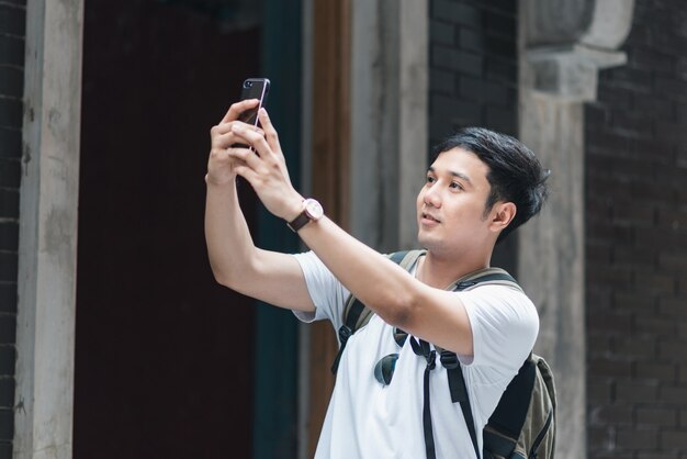 Hombre asiático viajero que usa un teléfono móvil para tomar una foto mientras pasa un viaje de vacaciones a Pekín, China