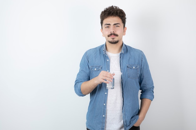 Hombre de aspecto serio sosteniendo un vaso de agua en blanco.