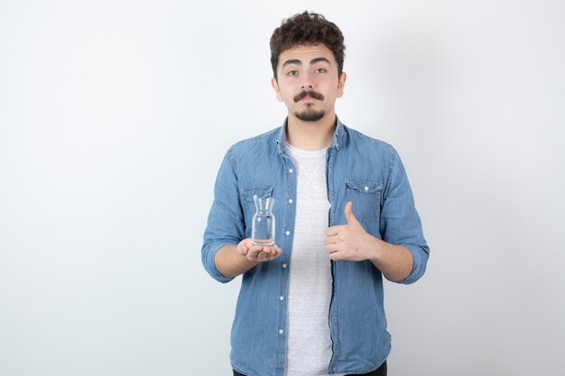 Hombre de aspecto serio sosteniendo un vaso de agua en blanco.