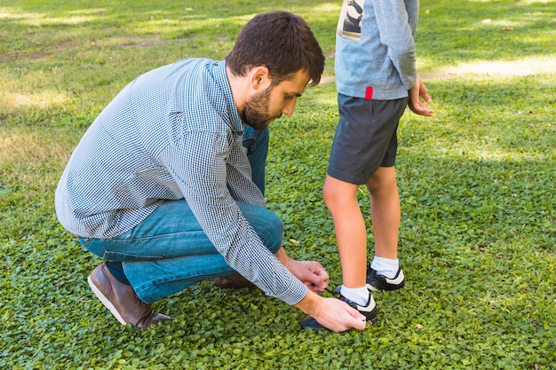 Un hombre atando el cordón de su hijo en el parque.